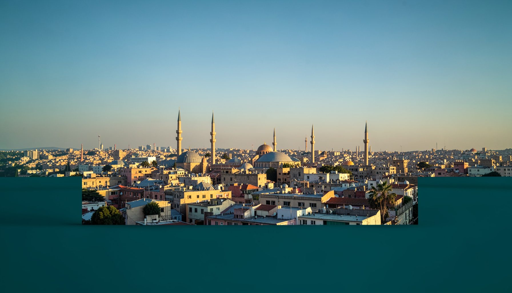لقطة جوية واسعة لمدينة عربية في ضوء المساء الذهبي، تظهر مآذن وأسطح منخفضة تمتد نحو الأفق تحت سماء صافية بلون أزرق مخضر خافت