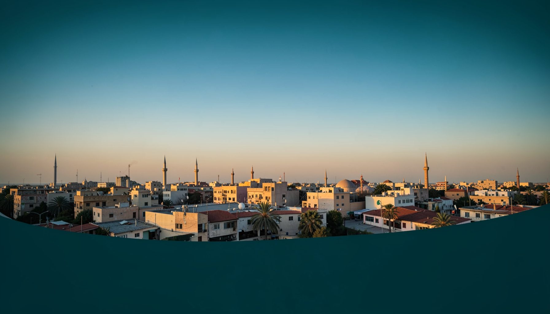 لقطة جوية واسعة لمنطقة ساجر في ضوء المساء الذهبي، تظهر مبانٍ منخفضة ومآذن تمتد نحو الأفق تحت سماء صافية